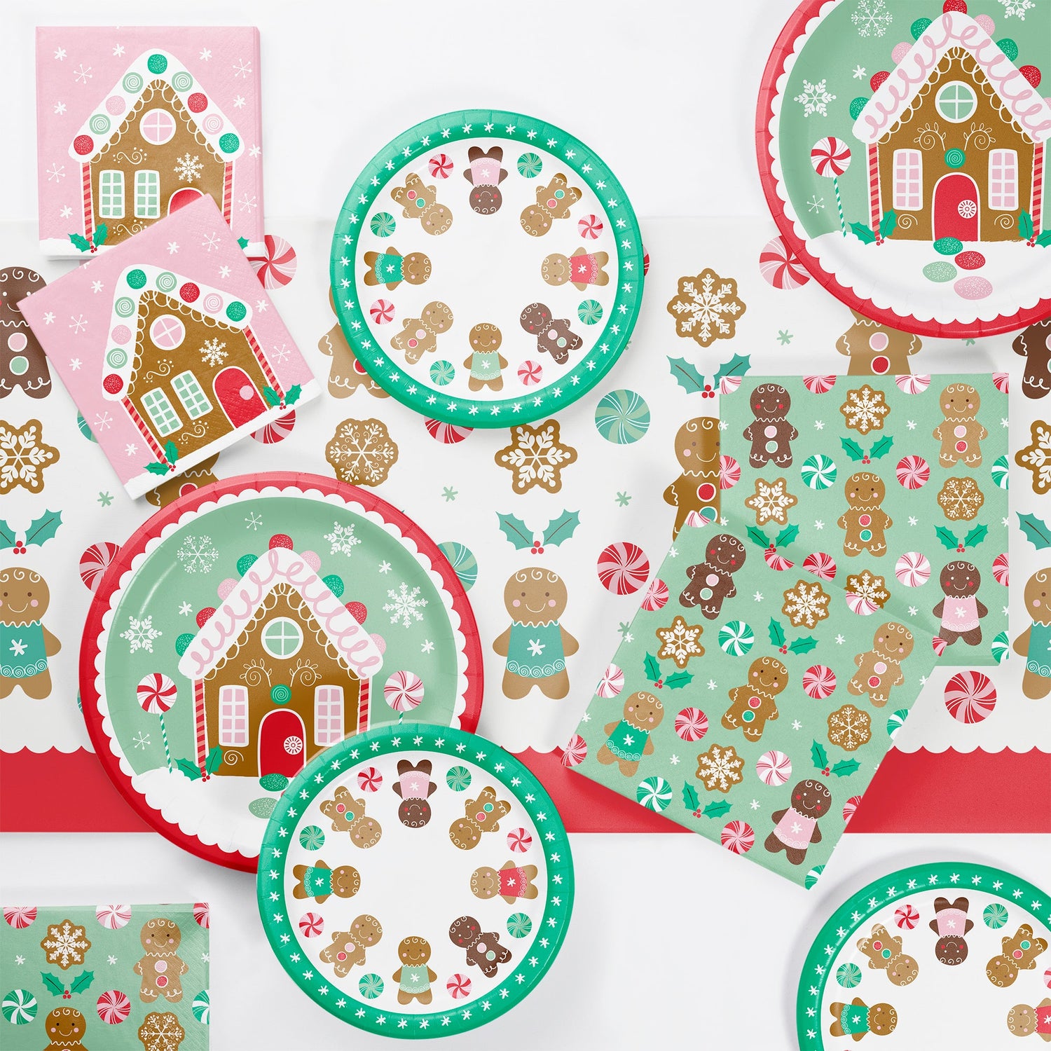 Christmas-themed paper plates, napkins and tablecloth with gingerbread house and candy cane designs on a white background.