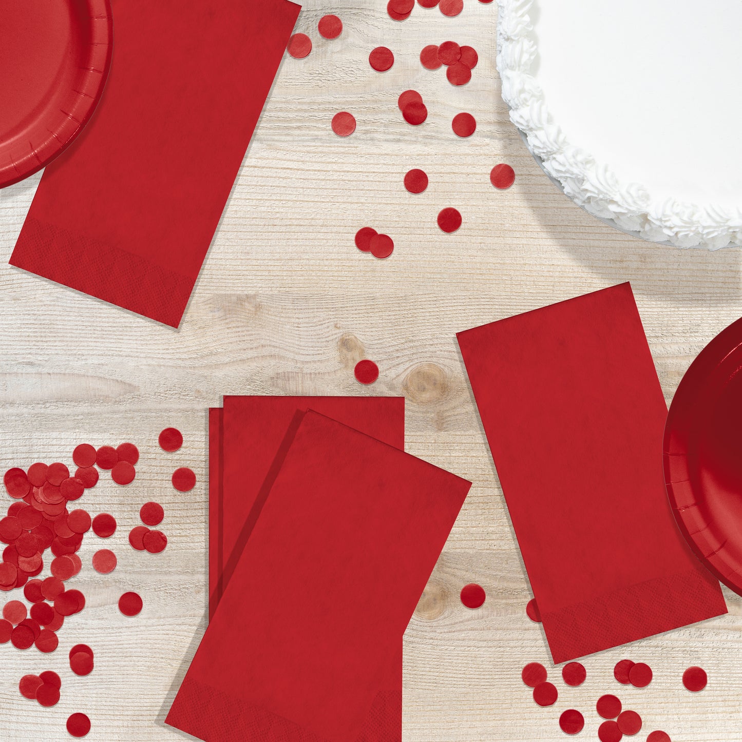 Red pin embossed guest napkins on a wood table with circle confetti