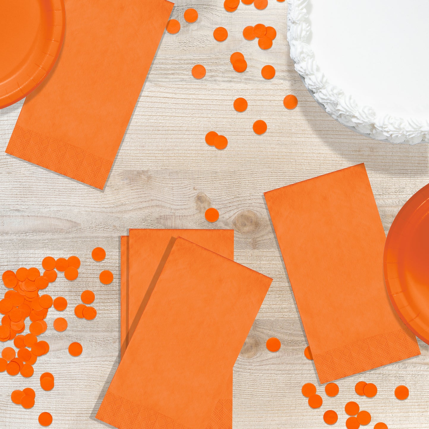 Orange napkins, plates and confetti on a wood background