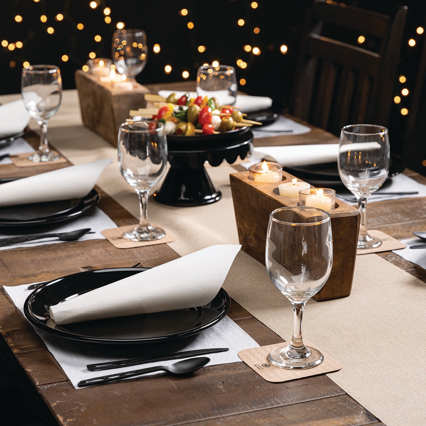 Elegant dinner table setting with wine glasses, plates, napkins, coasters and candles on a wooden table.