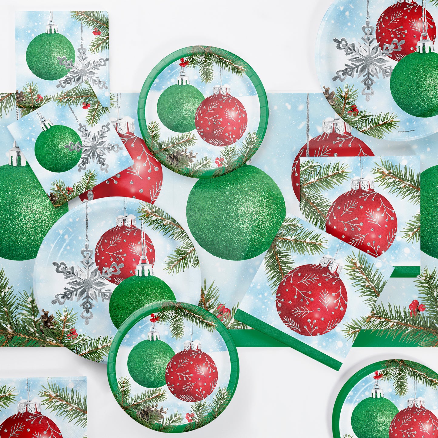 Paper napkins, plates and tablecloth with green glittery Christmas balls and silver snowflake ornament on a snowy branch