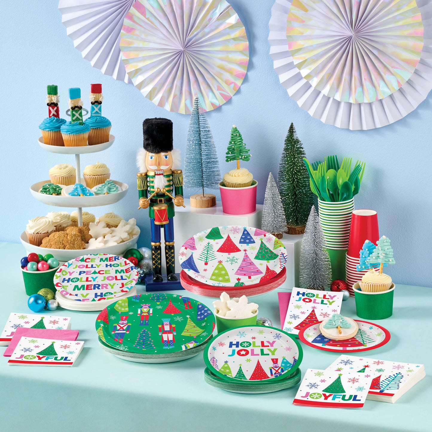 Joyful and Jolly Lifestyle tableware. Christmas-themed party table with decorations, food, and tableware on a light blue background.