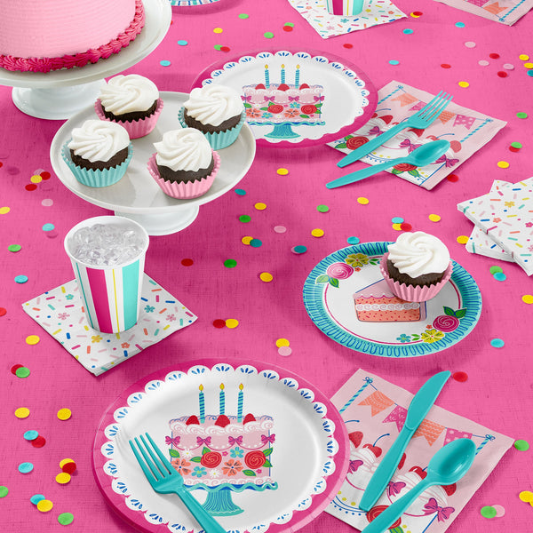 Pink and blue plates, napkins, cutlery on a pink tablecloth with cake and cupcakes
