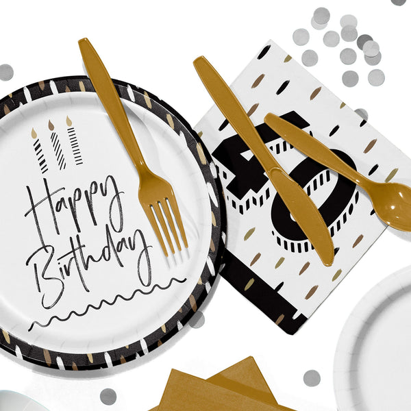 Flat lay of black, white, and gold birthday party tableware, including a paper plate that reads “Happy Birthday,” gold plastic cutlery, a napkin with a large “40,” and scattered silver confetti on a white background.