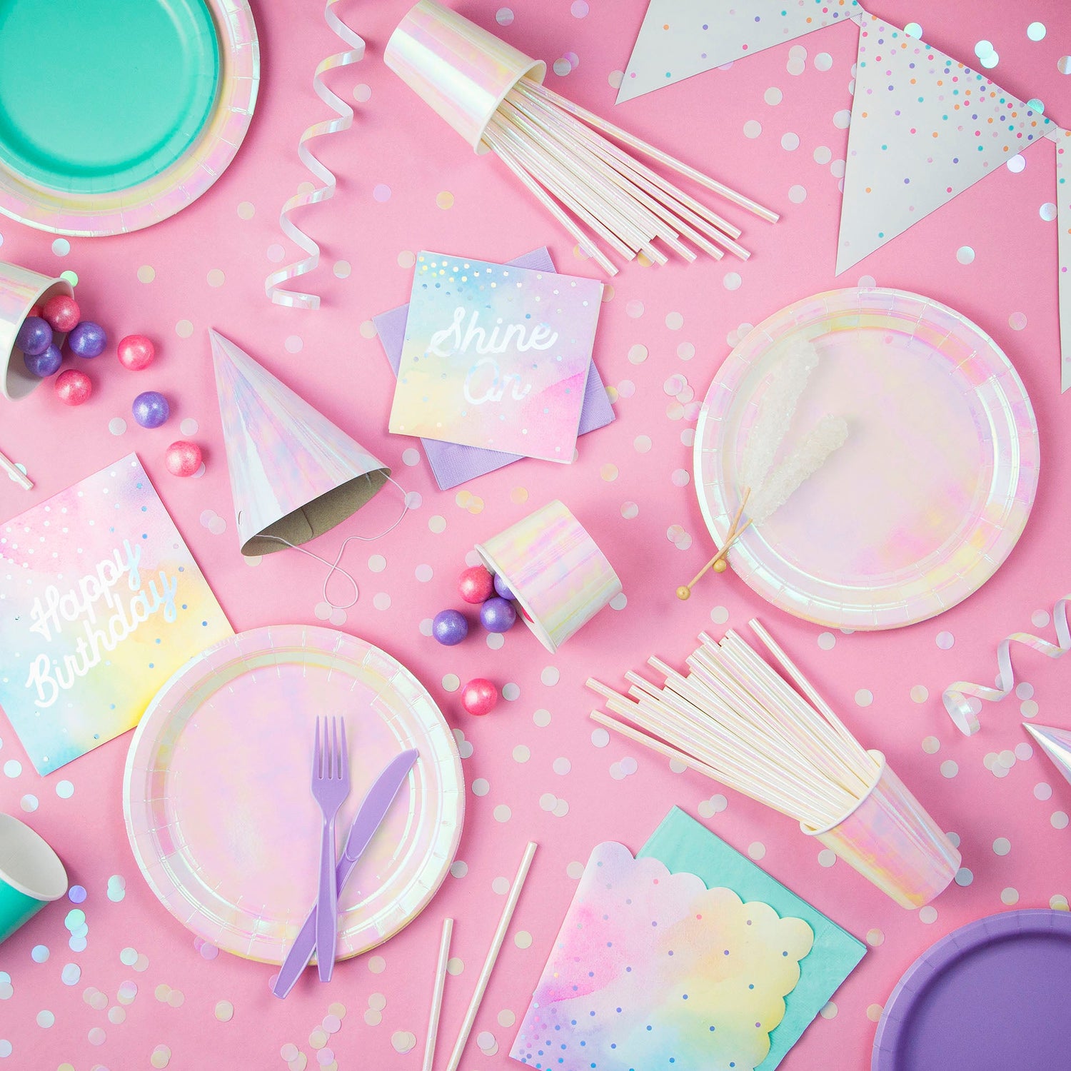 Iridescent Party Supplies. Iridescent plates, napkins, cups, party hats and confetti displayed on a pink background