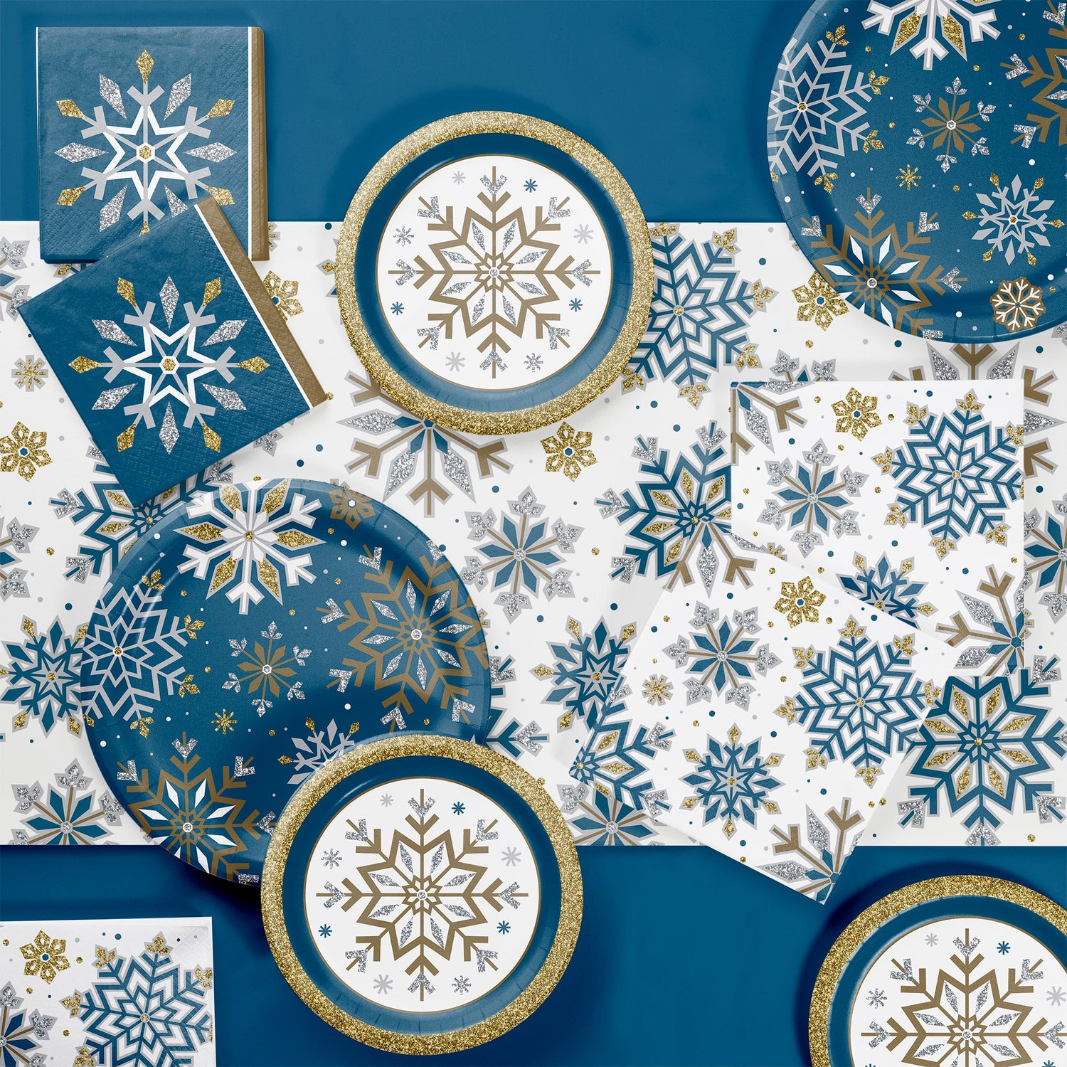 Paper napkins, plates and tablecloth with snowflake designs on blue, white, and gold background