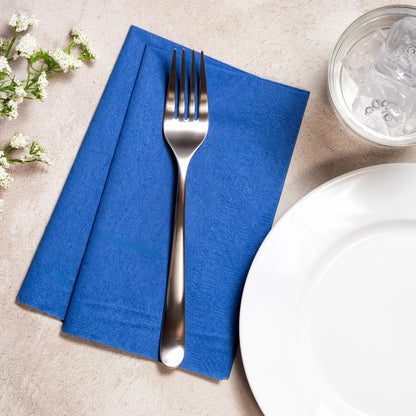 7.5" x 4.25" Regal Embossed Cobalt Blue Dinner Napkins 1000 ct displayed on a table with a fork, glass of water and a plate