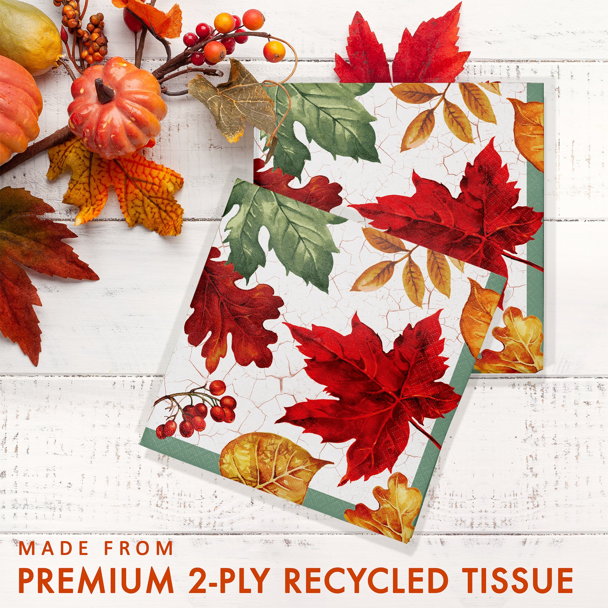 Autumn Air Luncheon Napkins 192 ct. Napkin with autumn leaf design on a white wooden surface with pumpkins and berries.