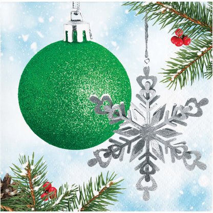 Paper napkin with green glittery Christmas ball and silver snowflake ornament on a snowy branch background