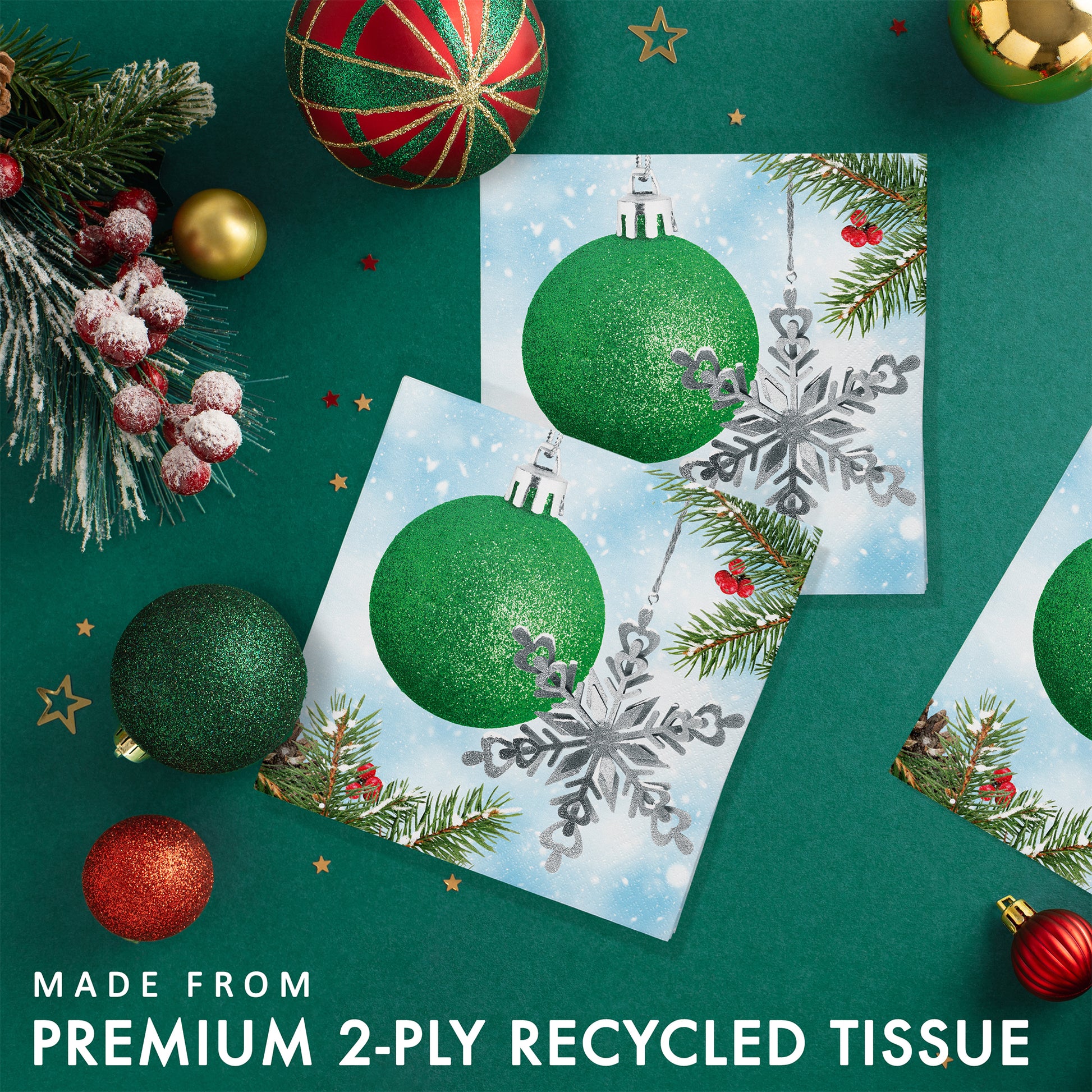 Paper napkin with green glittery Christmas ball and silver snowflake ornament on a snowy branch. Shown on a green background with Christmas ornaments and greenery.