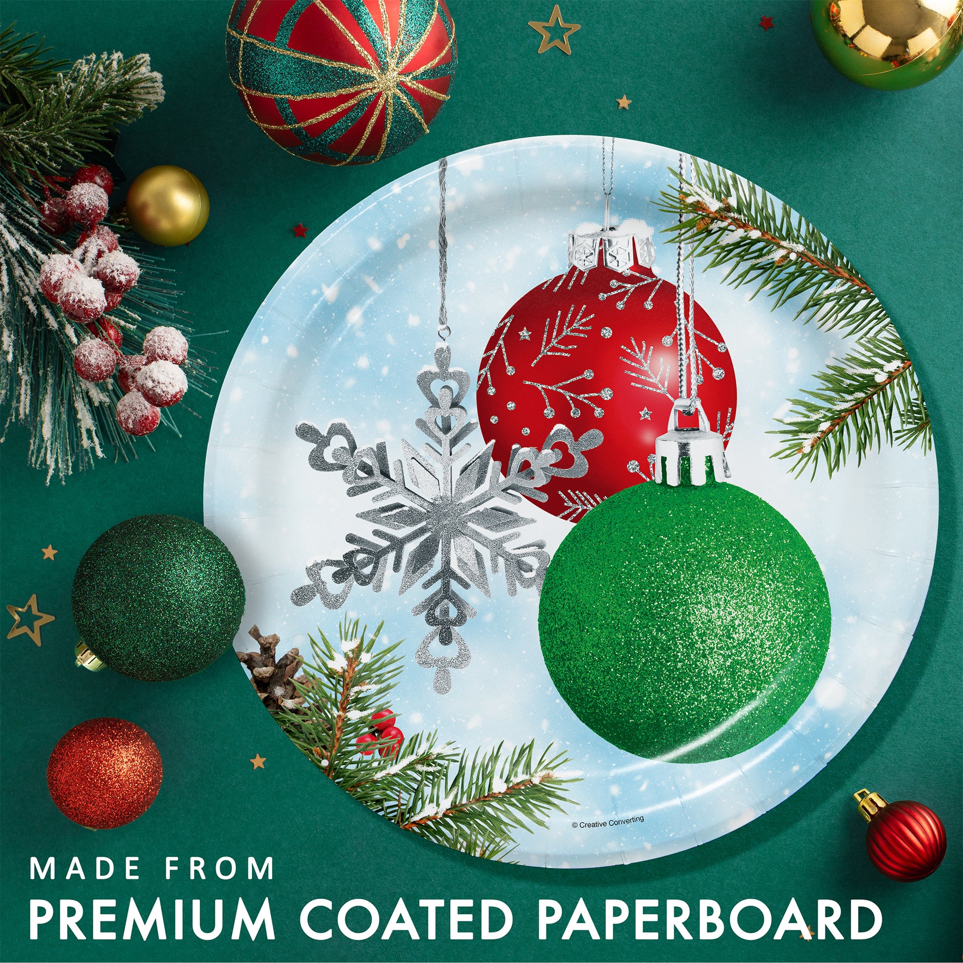 Decorative paper plate with Christmas ornaments on a green background with Christmas decorations and greenery.
