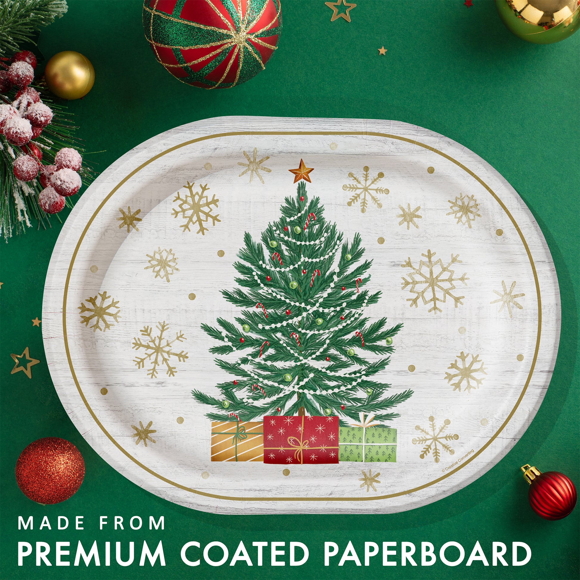 Decorative paper plate with a Christmas tree, presents and gold snowflakes on a white background. Plate shown on a green backgroun with festive decorations.