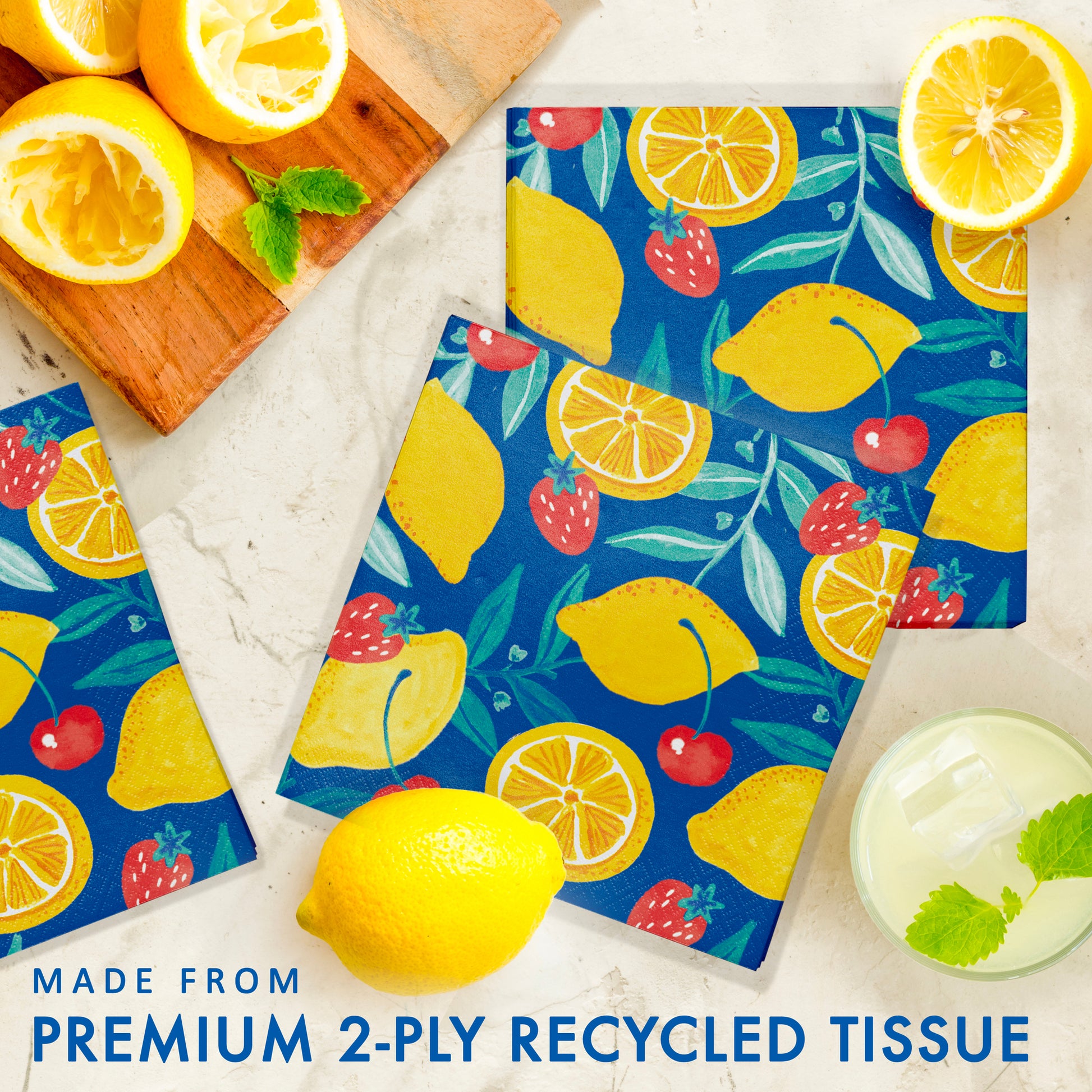 Colorful paper napkins with lemon, strawberry and cherry pattern on a white surface with lemons and mint leaves.