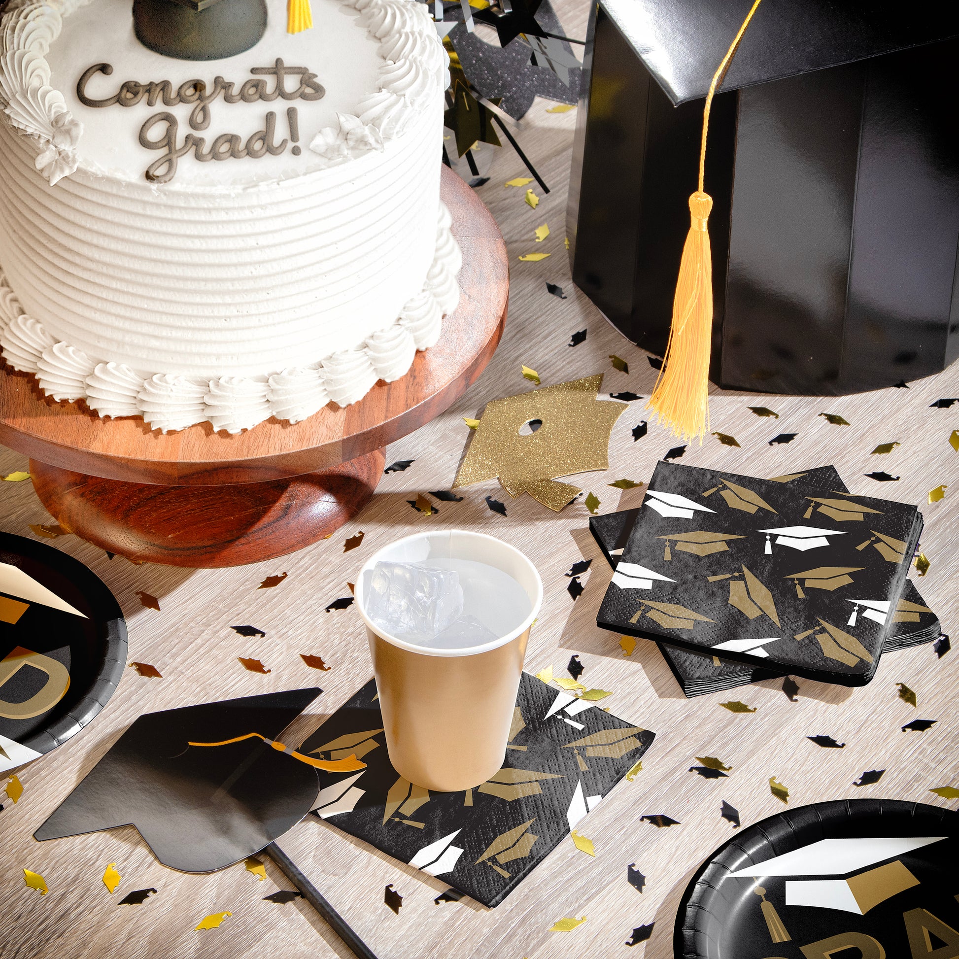 Graduation-themed table setting with cake, cap, napkins, and decorations on a wooden surface.