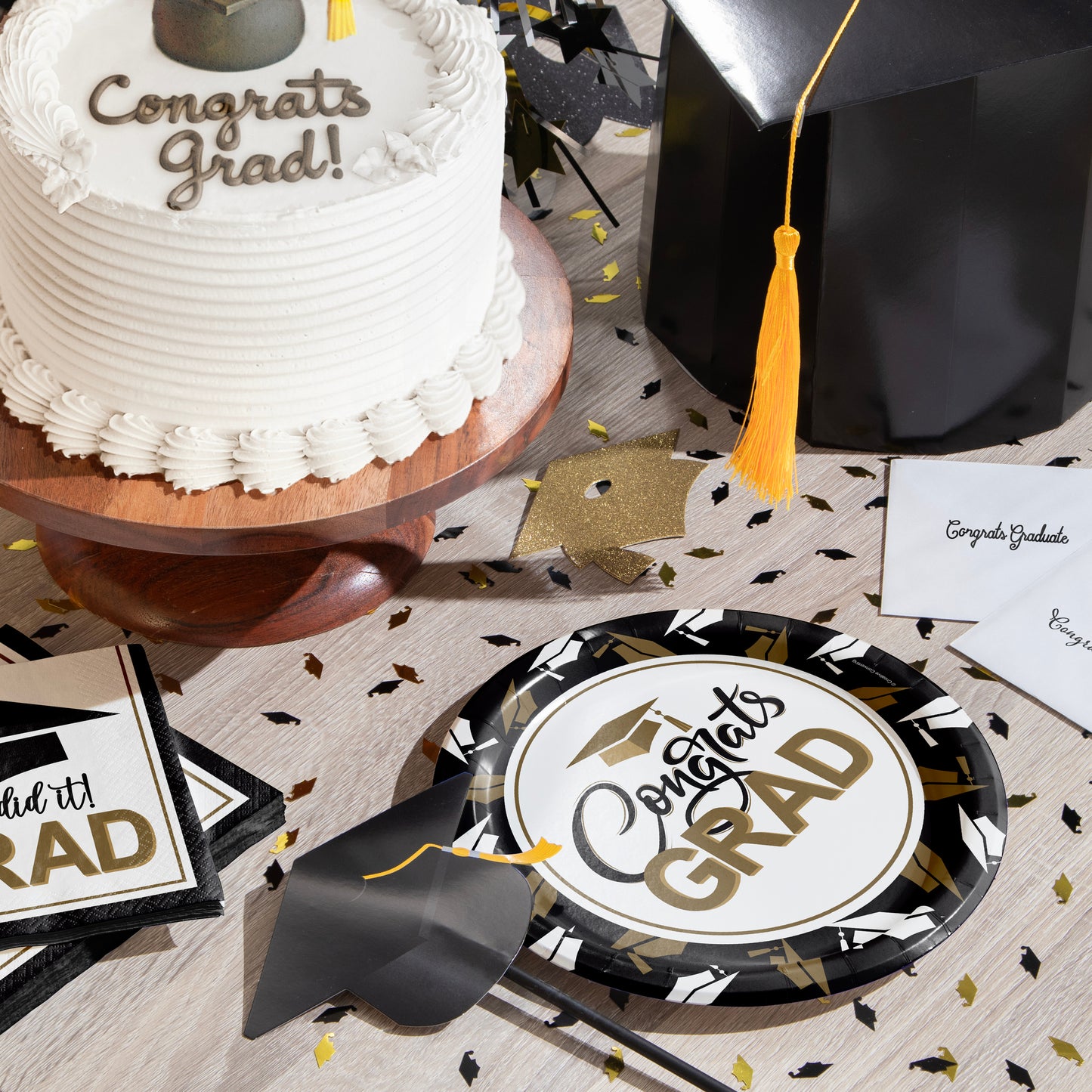 Graduation-themed table setting with cake, plates, napkins, and graduation decorations on a wooden surface.
