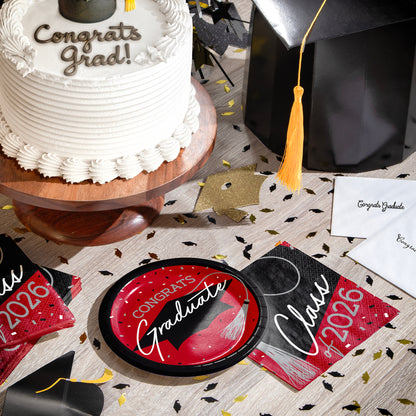 Graduation-themed items including a cake, plates, napkins and a graduation cap on a table.