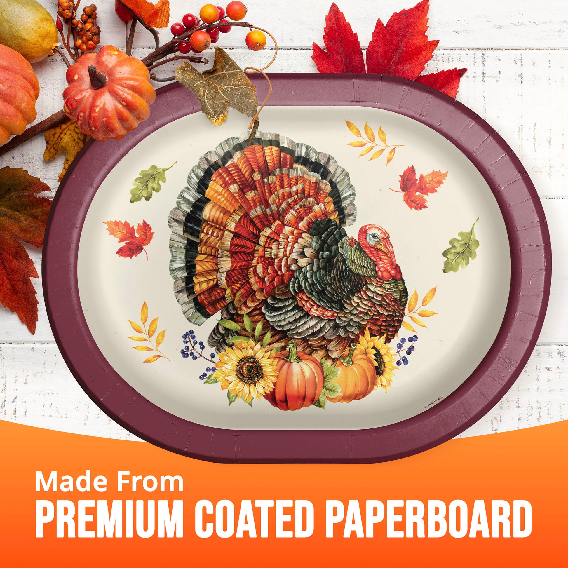 An oval Thanksgiving-themed paperboard platter with a printed turkey, pumpkins, sunflowers, and autumn leaves, shown on a white wood background with seasonal props and an orange banner reading 'Made From PREMIUM COATED PAPERBOARD'.
