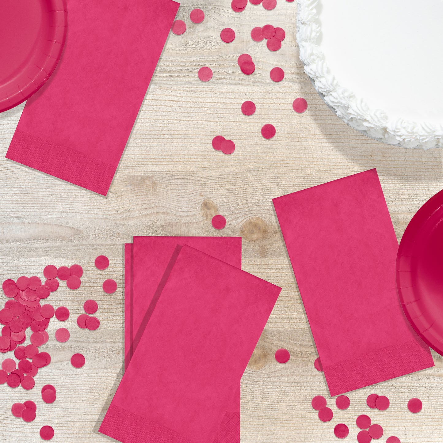 Pink paper plates and napkins with confetti on a wooden surface