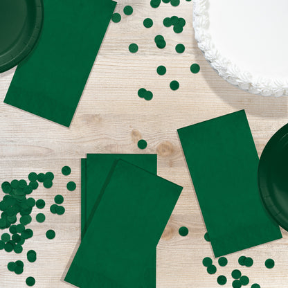 Green party supplies including napkins, plates, and confetti on a wooden table.