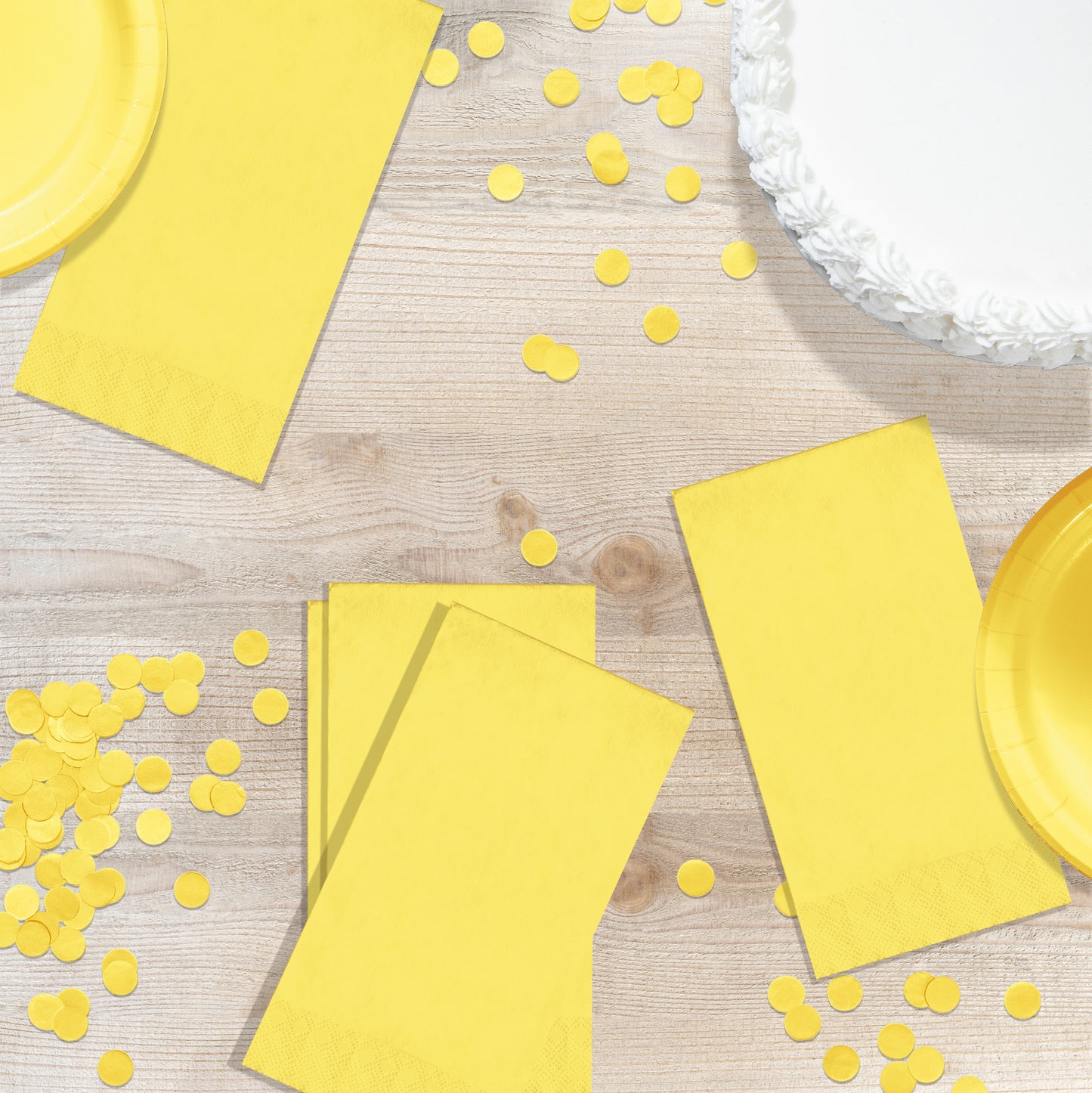 Yellow party supplies including plates, napkins, and confetti on a wooden surface.