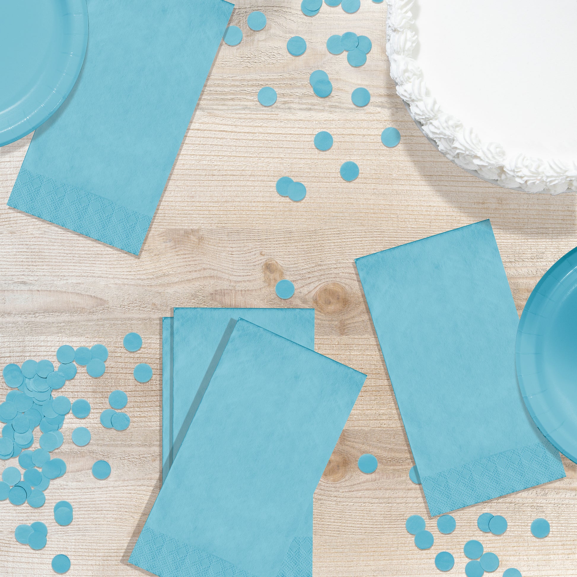 Blue party supplies including napkins and confetti on a wooden surface