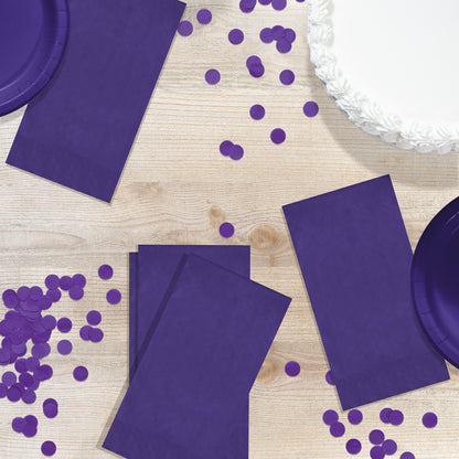 Purple party supplies including plates and napkins on a wooden surface with scattered purple confetti.