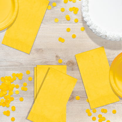 Yellow party supplies including plates and napkins on a wooden surface with scattered yellow confetti.