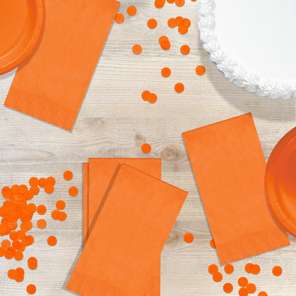 Orange napkins, plates and confetti on a wood background