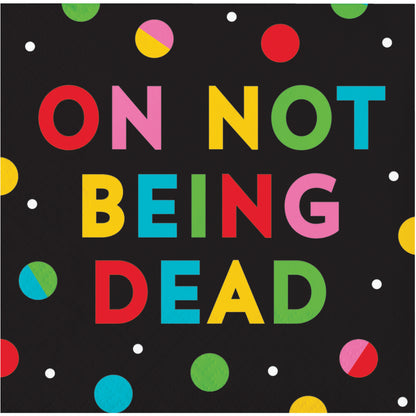 Napkin with colorful text 'ON NOT BEING DEAD' on a black background with polka dots.