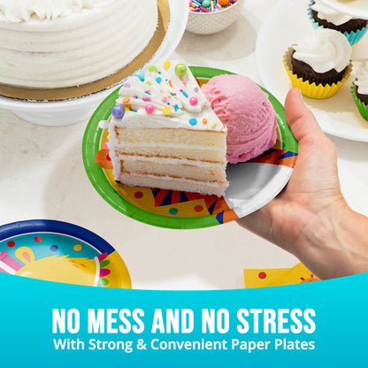 Hand holding a slice of cake with ice cream on a colorful paper plate, surrounded by more cake and ice cream.