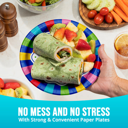 Colorful paper plate with a wrap and fruit, held by a hand, on a table with food.