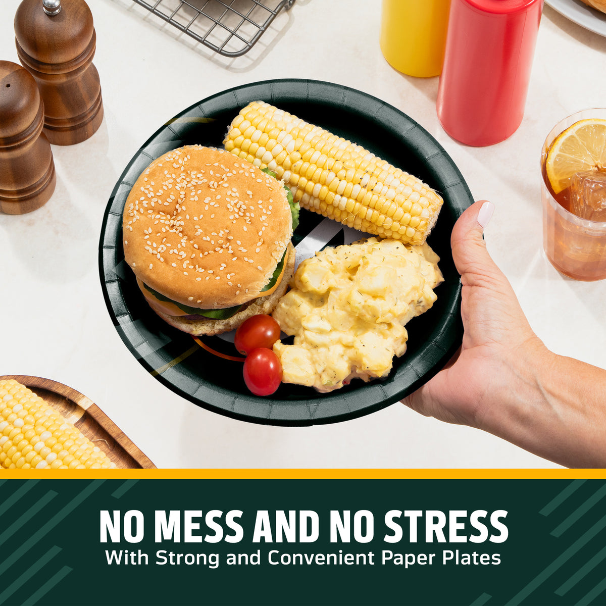 Hand holding a Green Bay Packers plate filled with a hamburger, corn on the cob, and potato salad. Banner with "No Mess and No Stress" text along the bottom