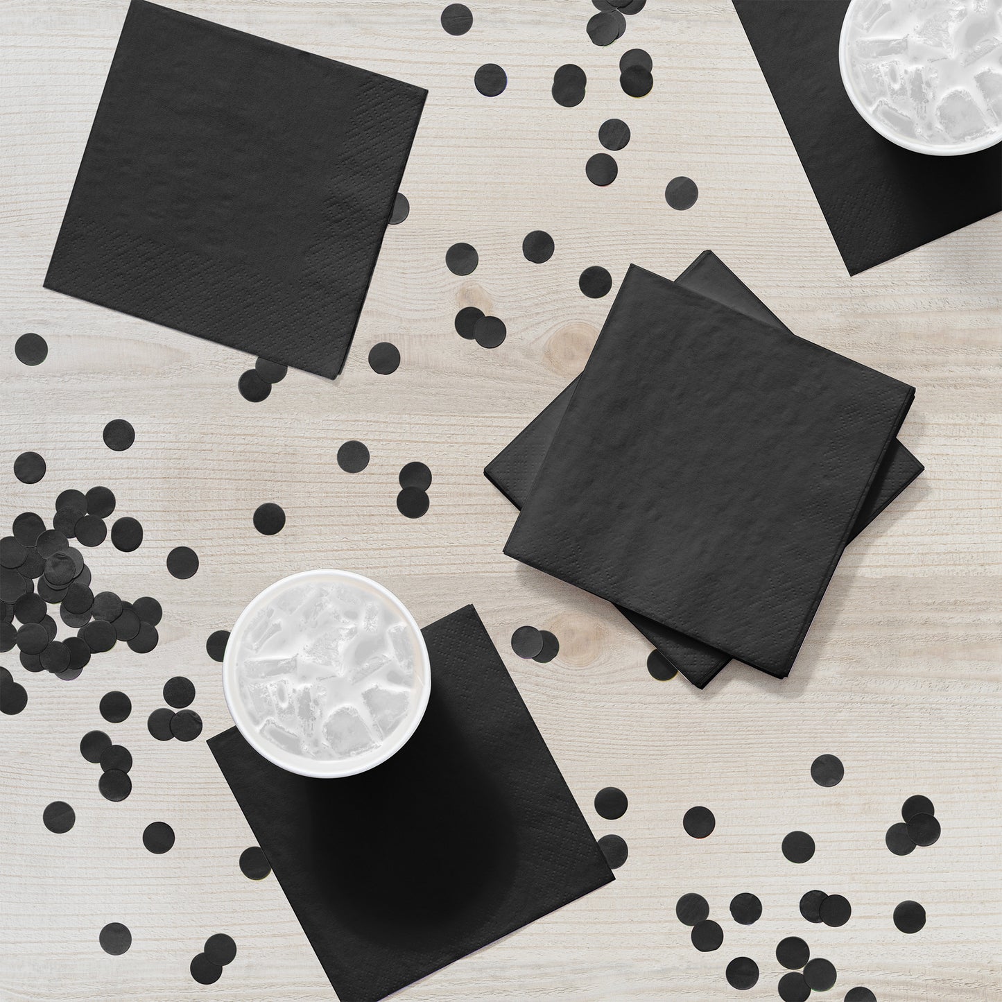 Black napkins and confetti on a light wooden surface