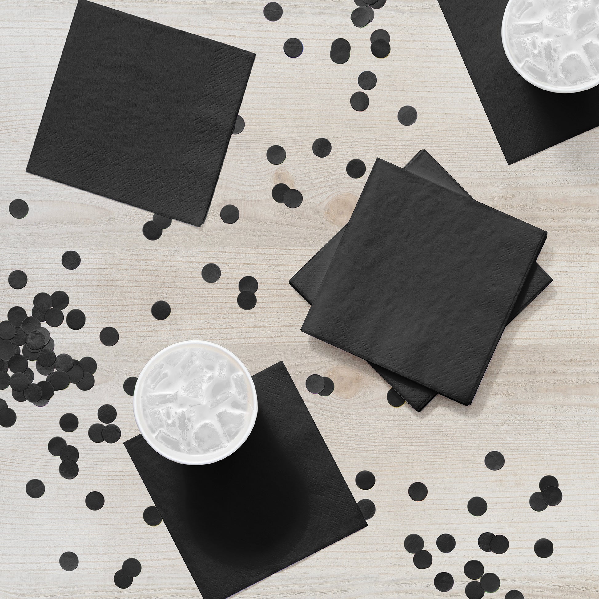 Black napkins and confetti on a light wooden surface