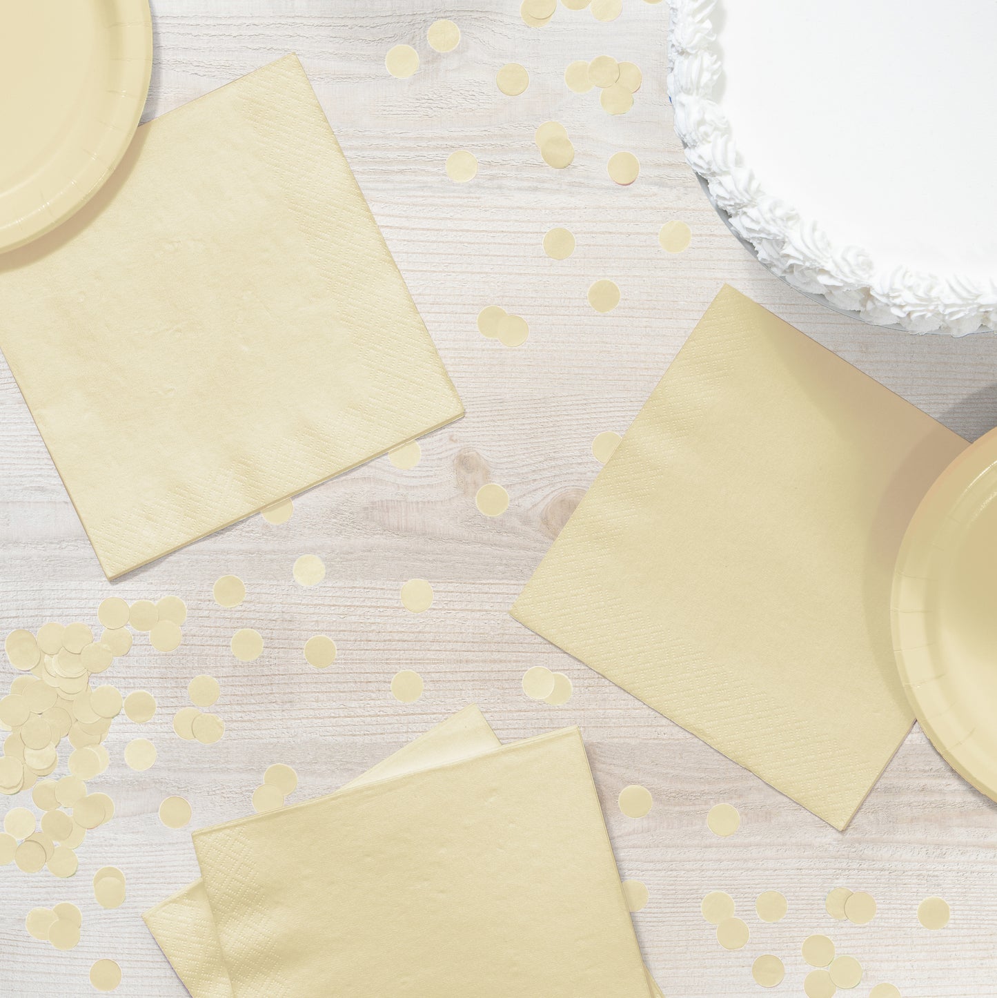 Ivory paper plates and napkins on a light wooden surface with scattered ivory confetti.