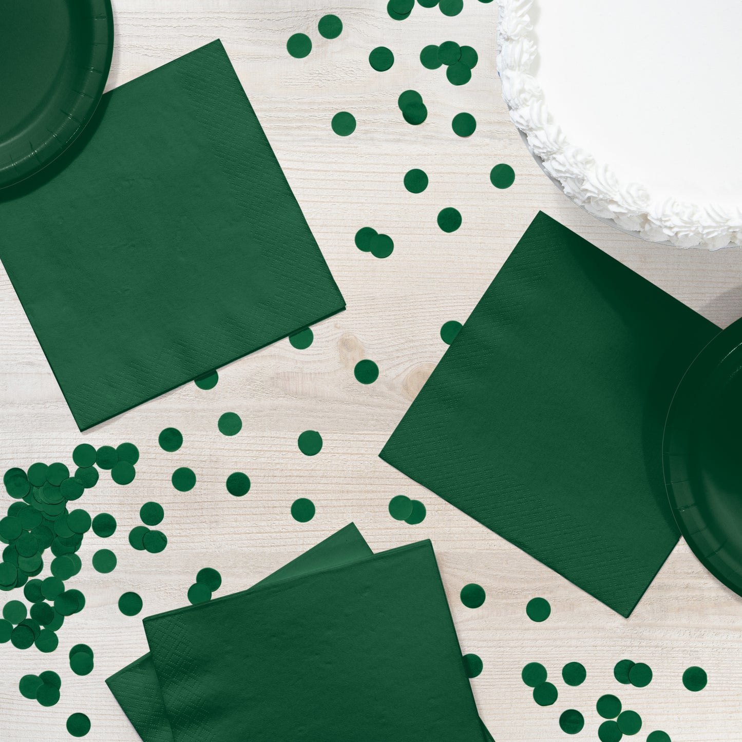 Green napkins and paper plates with green confetti on a light wooden surface