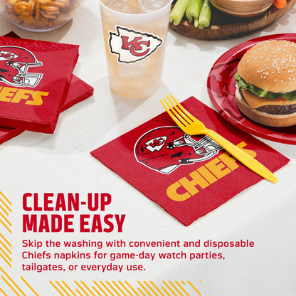 Red Kansas City Chiefs branded paper napkins with a football helmet logo and yellow 'CHIEFS' text, shown on a tabletop with a yellow plastic fork, a burger on a red plate, a drink cup, and promotional text.