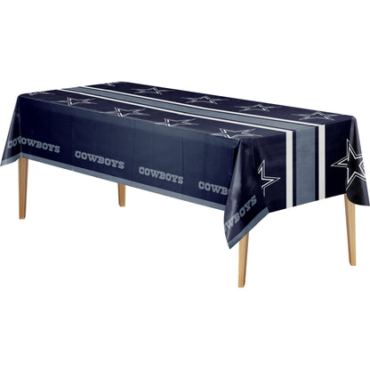 A Dallas Cowboys themed rectangular tablecloth in navy blue with white and gray logo patterns, shown draped over a table with wooden legs against a plain white background.