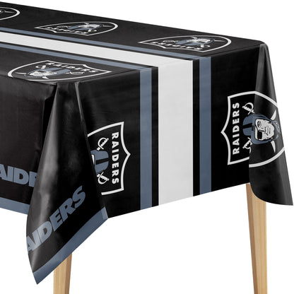 Close-up of a Las Vegas Raiders tablecloth with black background, white and silver Raiders logo, and "RAIDERS" text on a wooden table