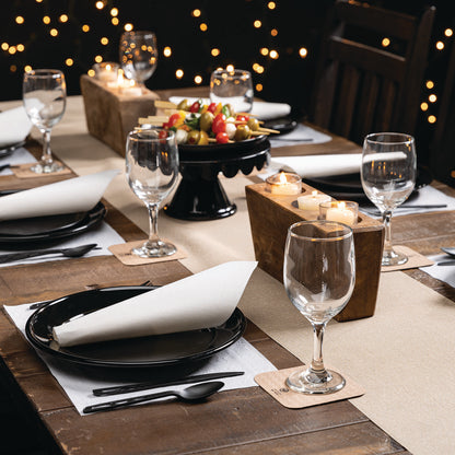Elegant dinner table setting with wine glasses, plates, napkins, coasters and candles on a wooden table.