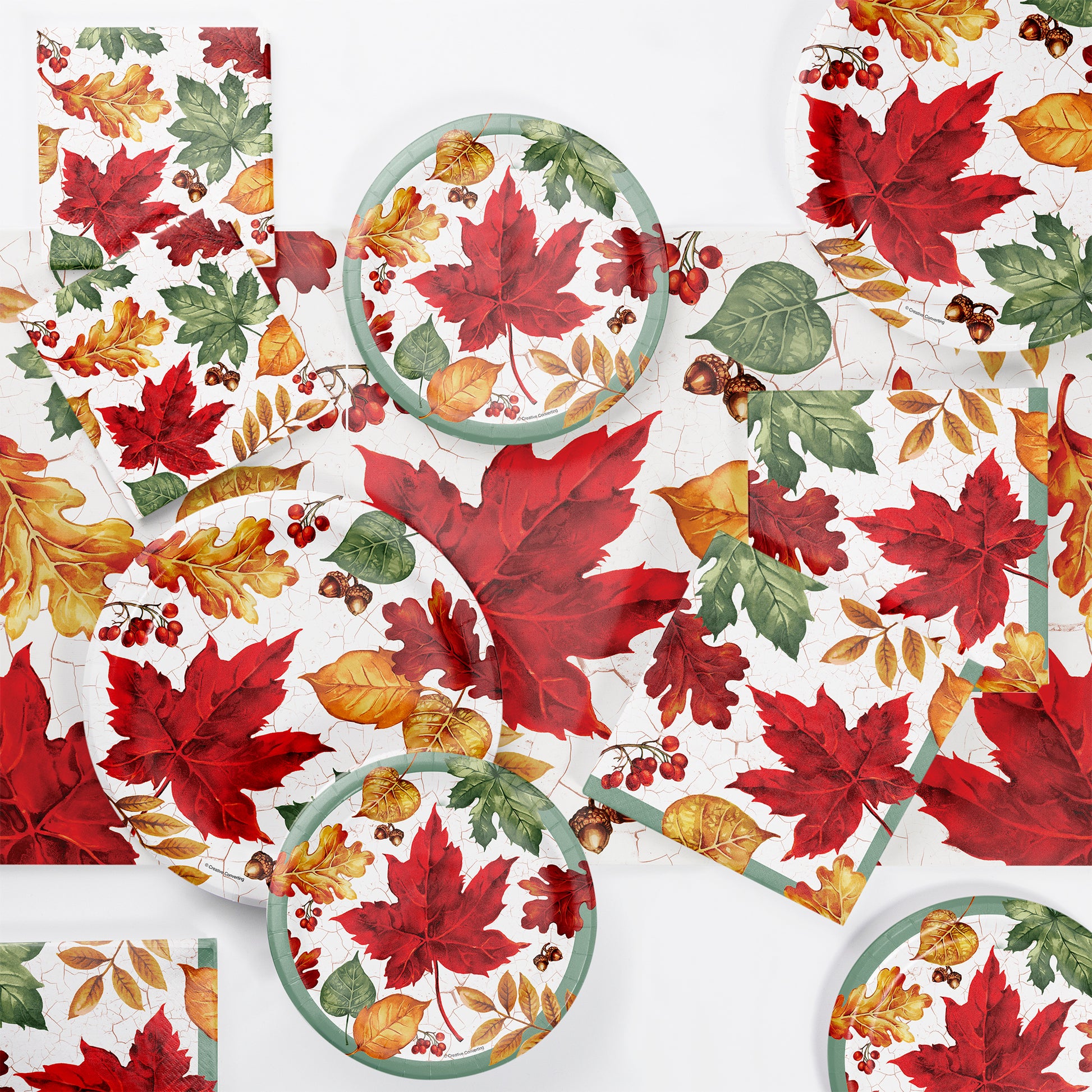 Autumn Air Paper Tablecloths 12 ct. Table setting with fall-themed paper plates and napkins featuring red, green, and yellow leaves on a white background.