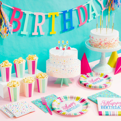 Birthday party setup with cake, candles, and colorful decorations against a turquoise wall.