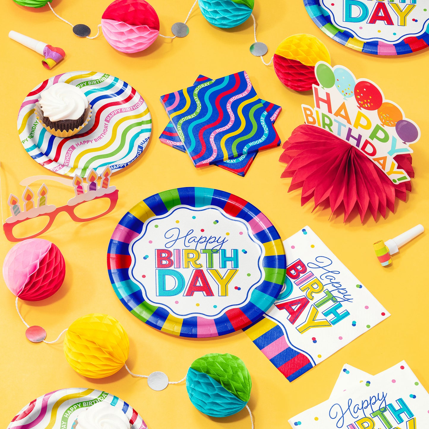 Colorful birthday party supplies including plates, napkins, and decorations on a yellow background.
