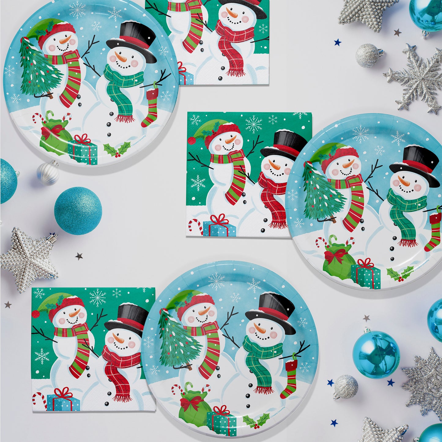 Christmas-themed plates and napkins with snowmen and winter decorations on a white background.