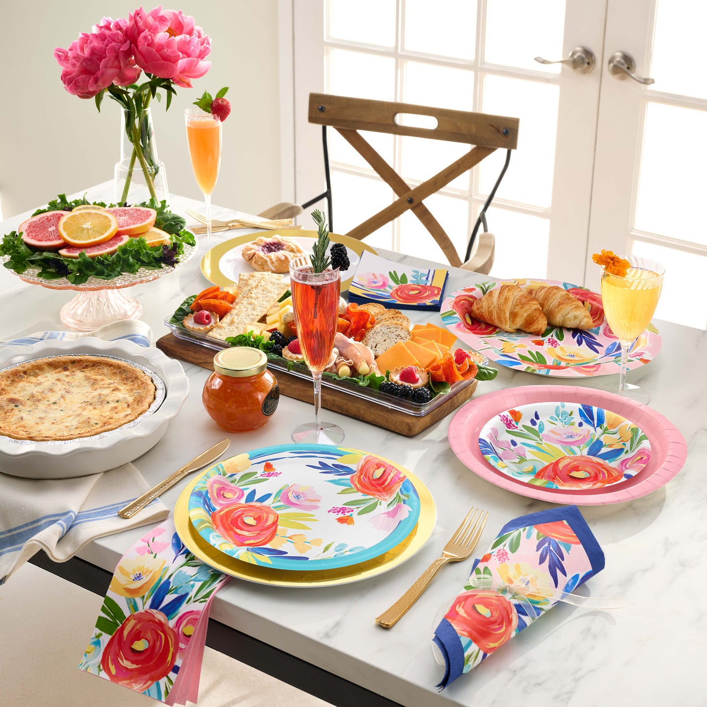 Dining table set with floral plates, glasses, and food on a marble surface.
