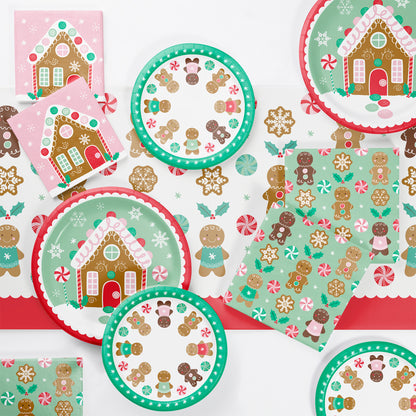 Christmas-themed paper plates and napkins with gingerbread men, gingerbread houses and candy cane designs on a white background.