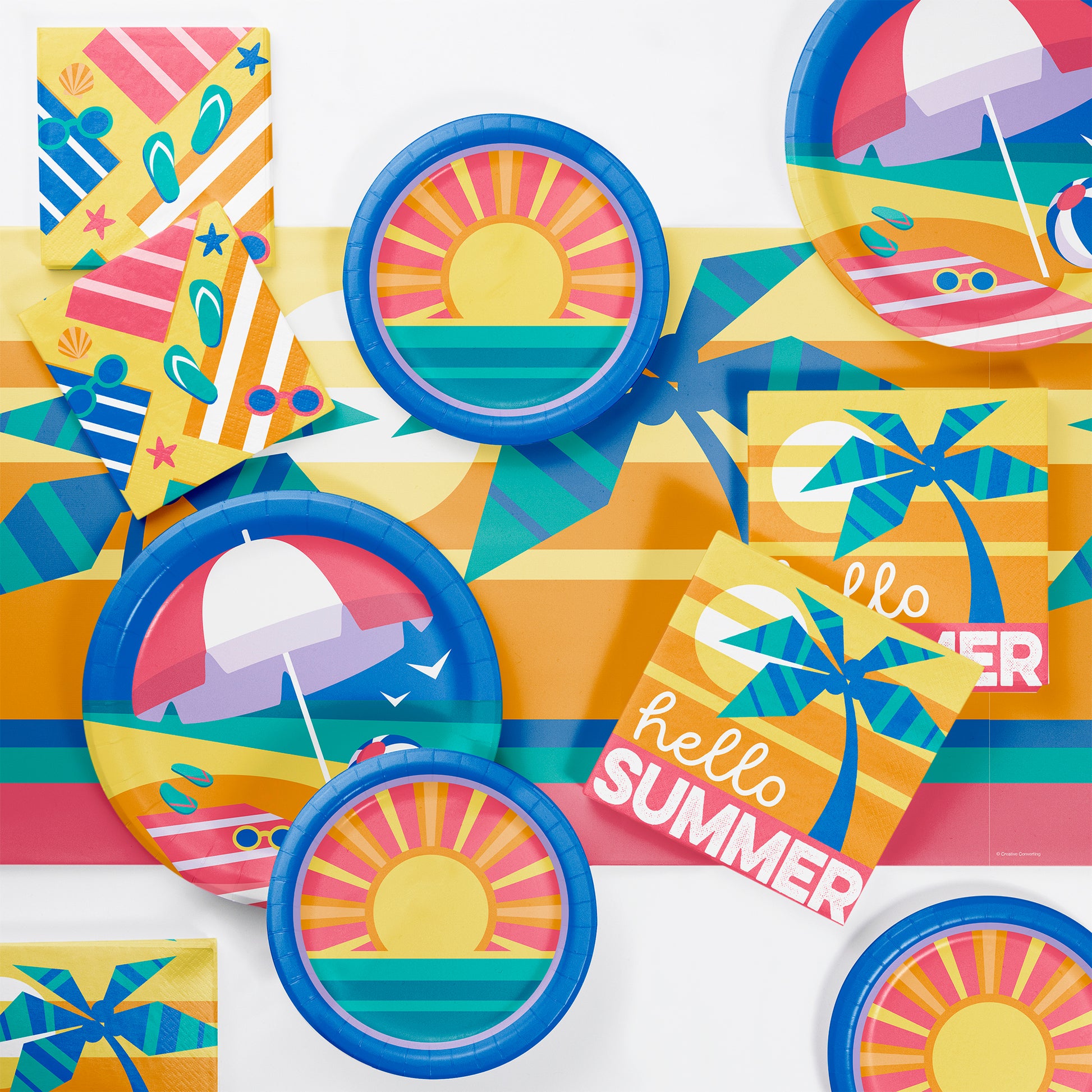 Colorful summer-themed party supplies including plates, cups, and napkins on a matching tablecloth.