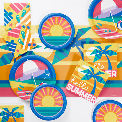 Colorful summer-themed party supplies including plates, cups, and napkins on a matching tablecloth.