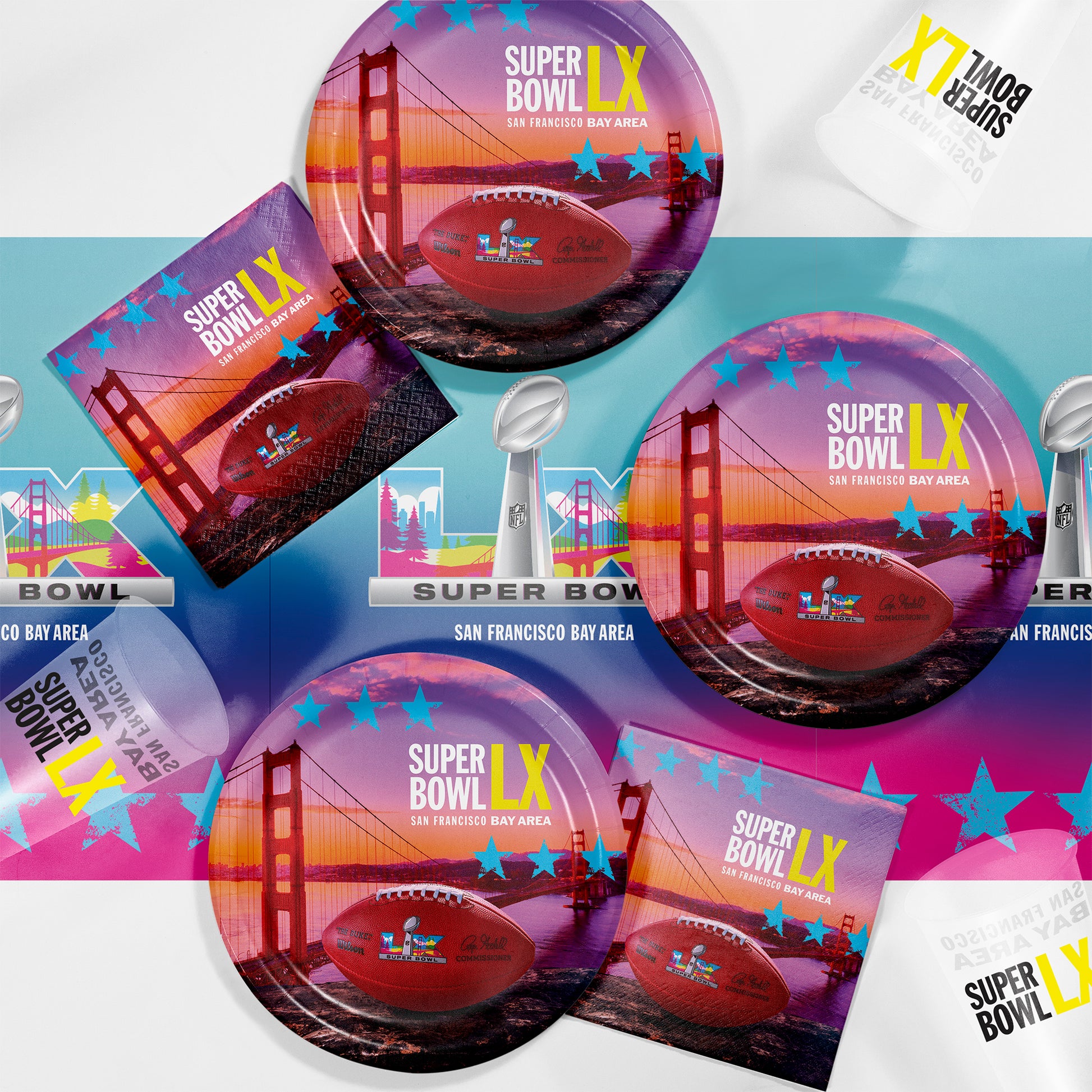 Super Bowl LX promotional graphic shown on paper napkins, paper plates, plastic cups and plastic tablecloth with a football and the Golden Gate Bridge in the background