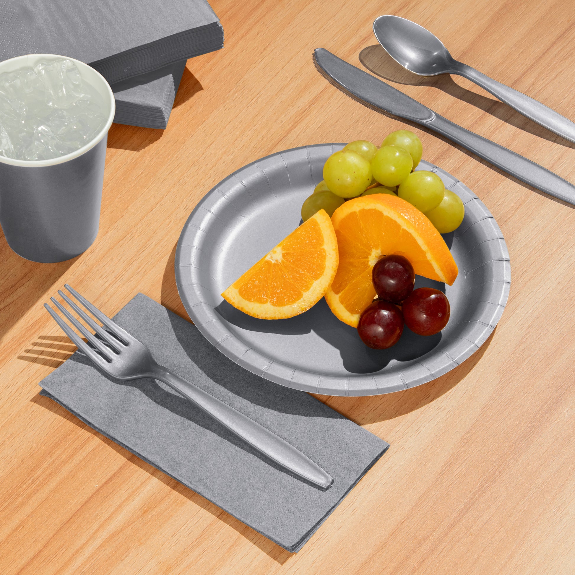 Silver plate with fruit, silverware, and a cup on a wooden table